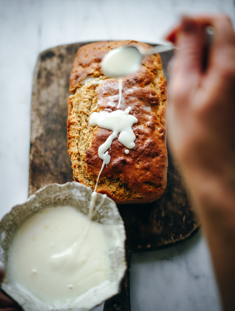 Drizzling pineapple glaze onto a fresh loaf of bread.