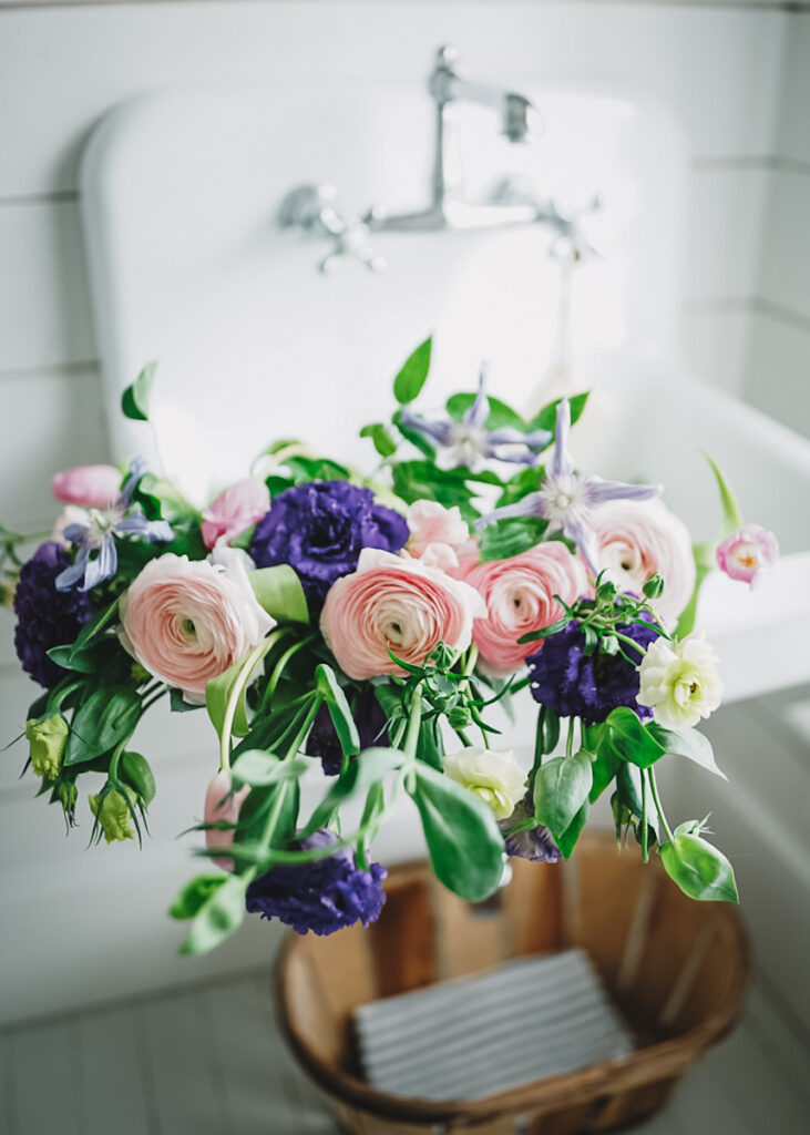 A bundle of pink ranunculus and sweet pea flowers in a sink being soaked and prepped for an arrangement.