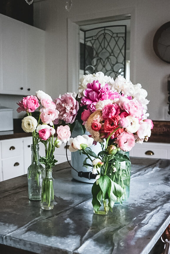 Beautiful arrangement of anemones and peonies in pastel colors and different vases.