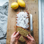 Lemon poppy seed bread just glazed on an antique cutting board with lemons.