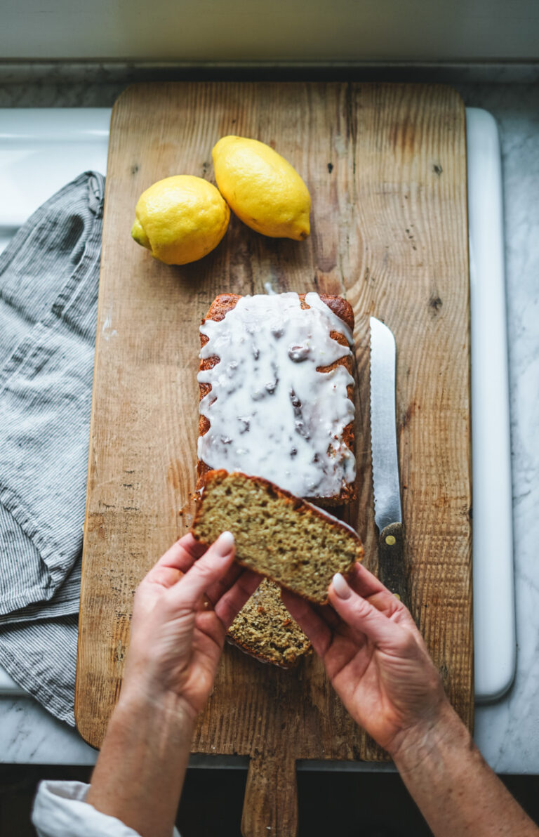 Lemon poppy seed bread just glazed on an antique cutting board with lemons.