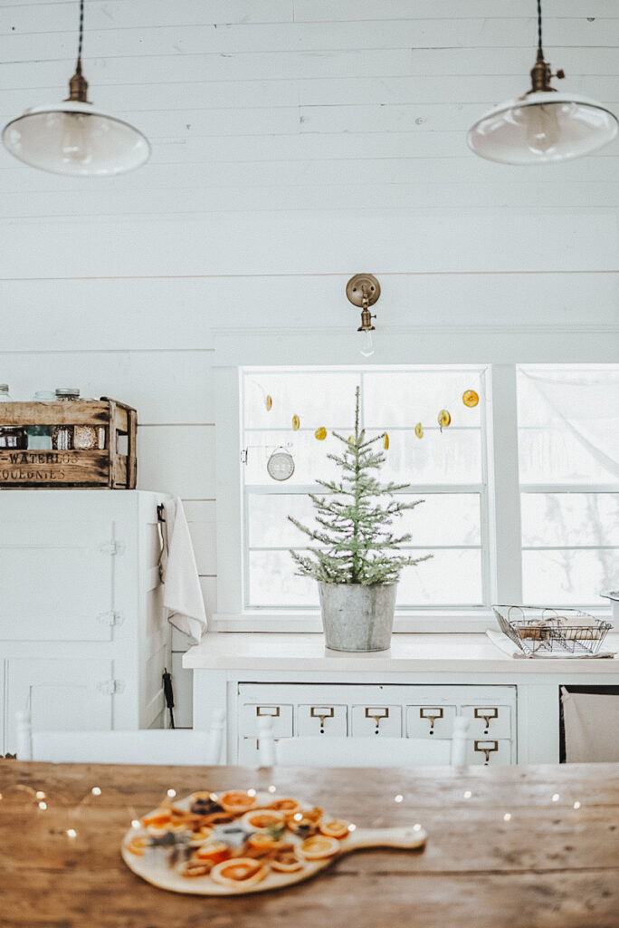 A beautiful kitchen at a cabin decorated for Christmas in white with dried orange garland and twinkle lights.