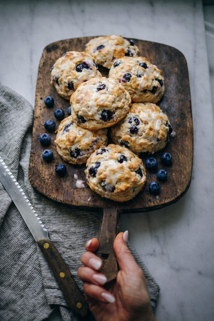 Blueberry scones being served on a vintage wooden tray with blueberries around them.