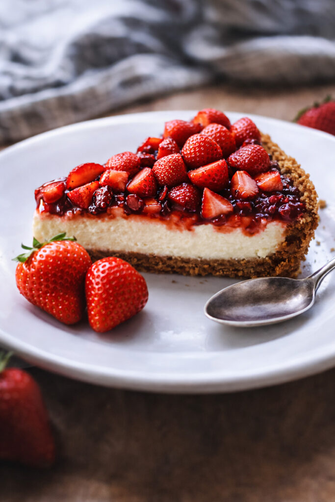 Slice of strawberry cheesecake on a weight plate with a spoon and some extra strawberries on the side. 