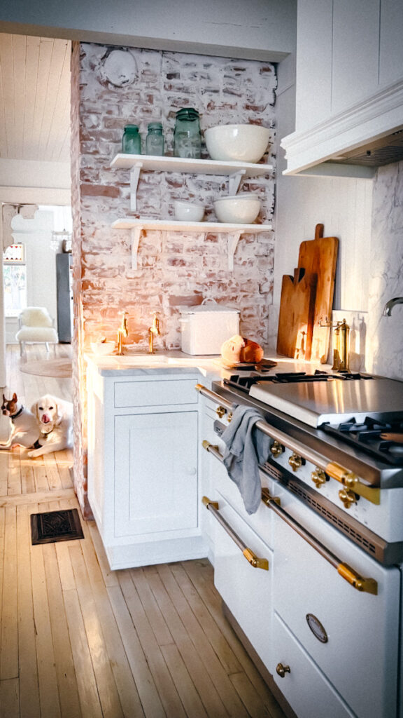 A white Lacanche French stove in a kitchen with marble countertops and open shelves. 
