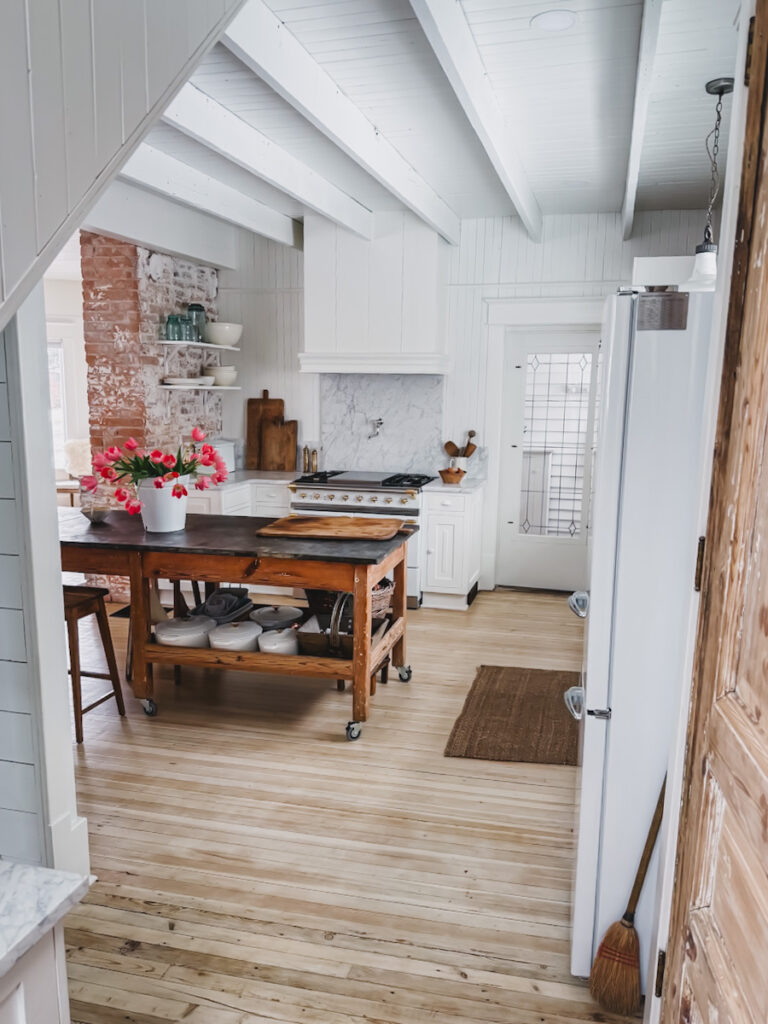 A vintage simplicity style kitchen with lots of antique rustic items and a bucket of fresh tulips on the kitchen island .