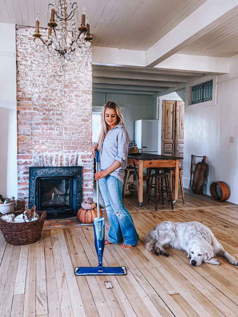 Deborah cleaning her floors in front of her fireplace and kitchen with an eco-friendly spray mop. 