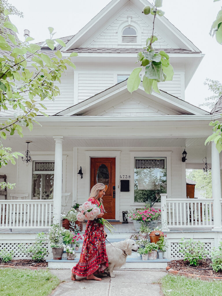 1903 Queen Anne Victorian-style home with fresh flowers on the front porch and a girl walking her dog .