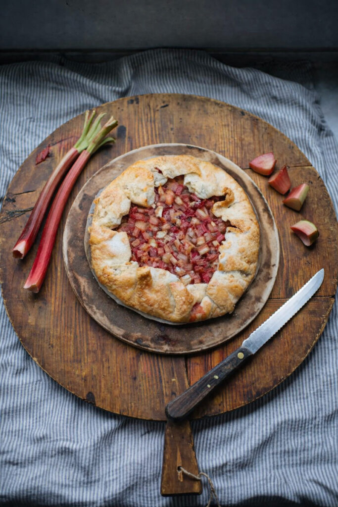 Rustic Rhubarb Galette on a rustic wooden cutting board with chunks of rhubarb beside it. 