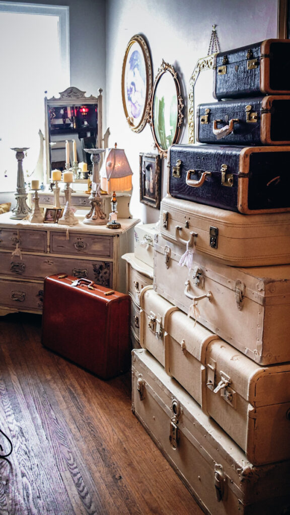 A beautiful antique shop that has a stack of vintage suitcases seven high and a beautiful white vintage dresser
