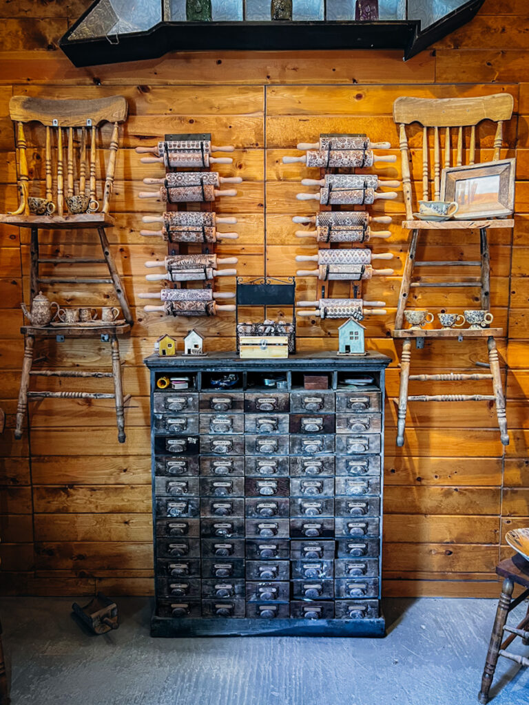 A stunning apothecary cabinet that is rustic, with antique chairs hanging beside it on the wall