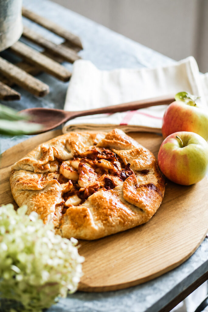 An apple galette that has just been baked and placed on a cutting board with a golden brown crust. 