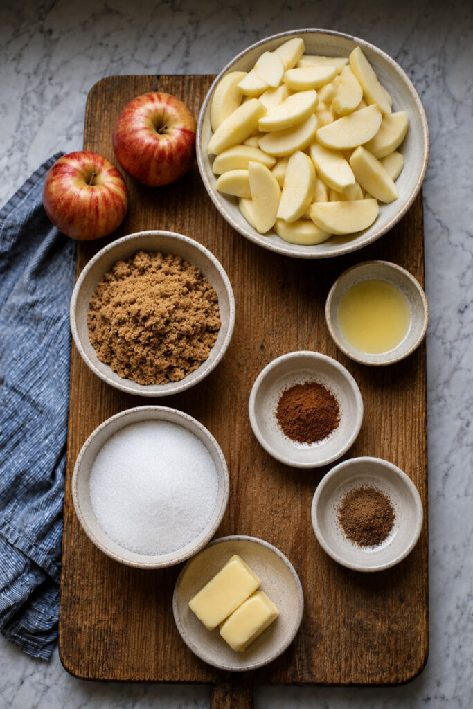 Ingredients used to make an easy apple crumble, such as: sliced apples, butter, cinnamon, cardamom, brown sugar, and oats.