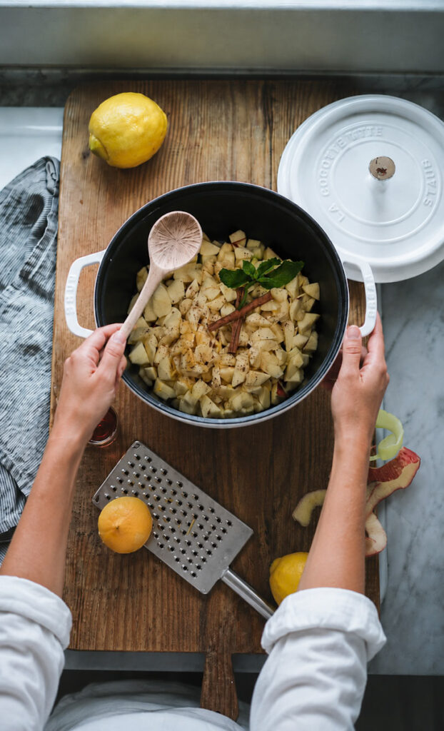 Mixing the cinnamon sticks, mint, apples, and cardamom together in a large pot to make apple crumble 