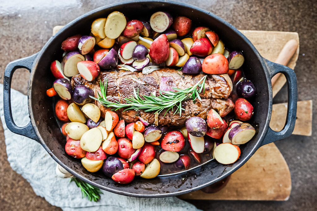 A delicious roast beef with colorful roast potatoes and a rosemary sprig, perfect for fall dinner in a cast-iron dish.