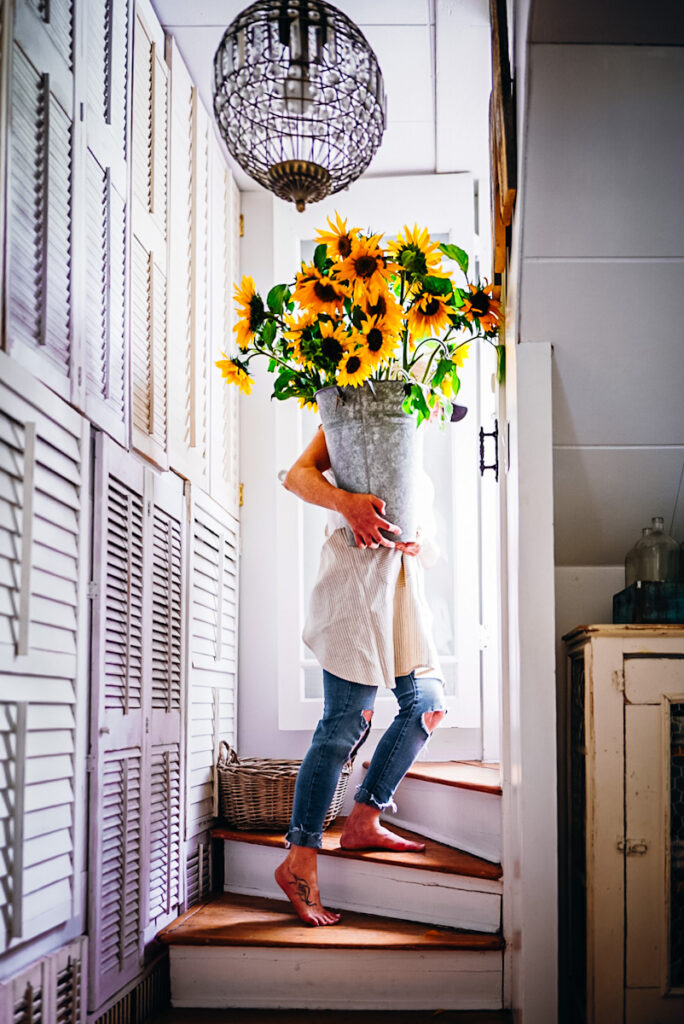 A girl carrying a huge bundle bouquet of sunflowers up the staircase in a galvanized vintage bucket.