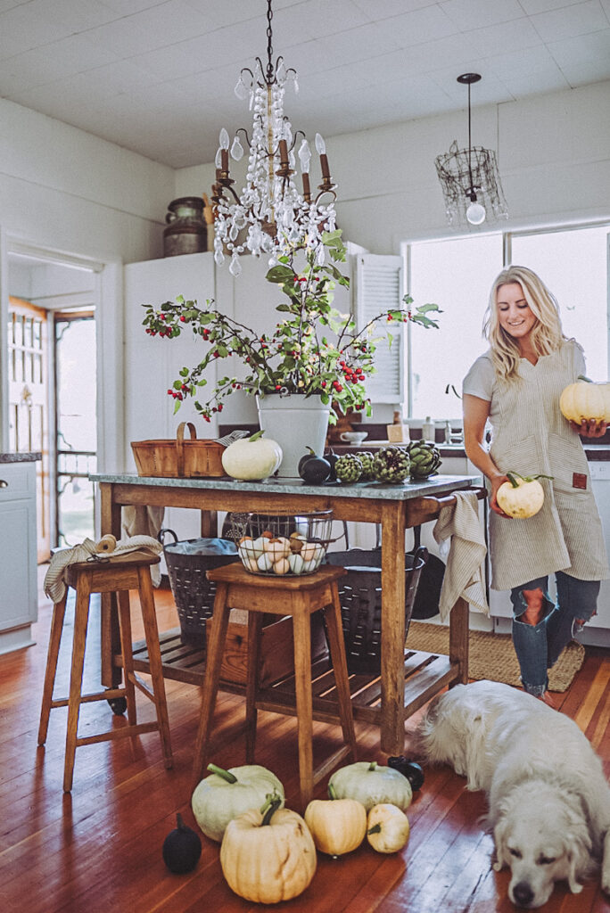 Deborah from B Vintage Style embracing Hygge in autumn by carrying pumpkins and decorating her kitchen with apple tree branches, artichokes, and colorful eggs in baskets.