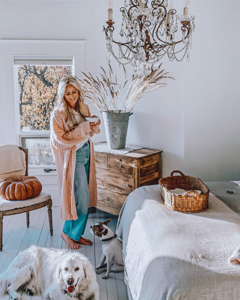 Deborah in her bedroom with fall decor like pumpkins and bunches of dried grasses relaxing with her dogs.
