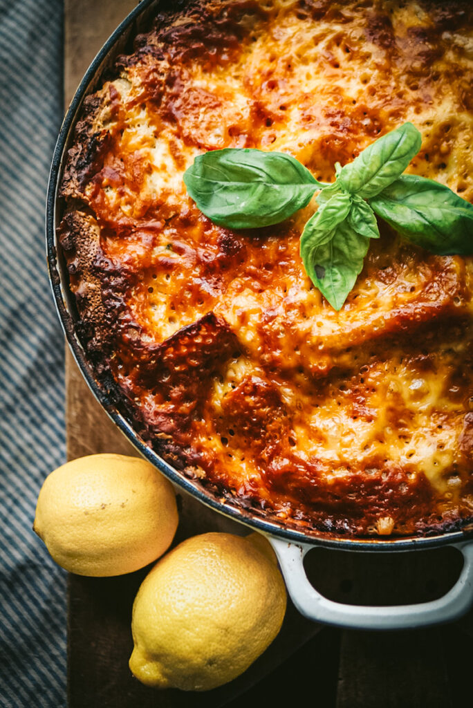 Delicious lasagna with basil on top baked for fall dining with two lemons on an antique cutting board.