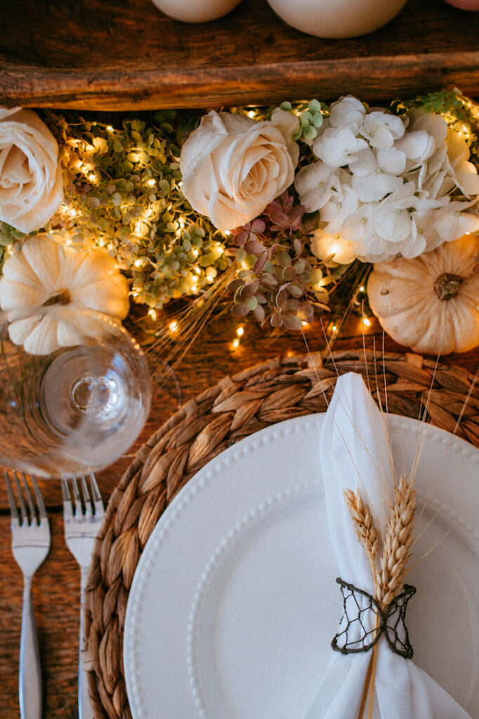 Twinkle lights in the centerpiece with white pumpkins, dried hydrangeas, and a table setting that has wheat springs.