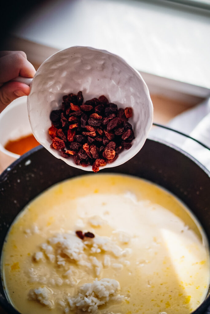 Adding raisins into the cast iron pot to make baked rice pudding.