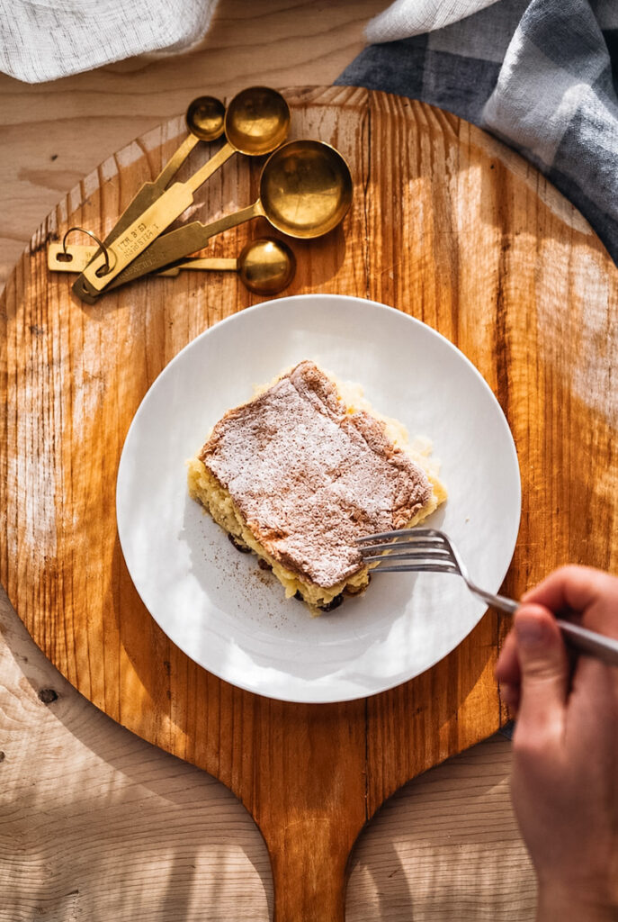 A slice of rice pudding ready to eat on a white plate in front of a sunny window.