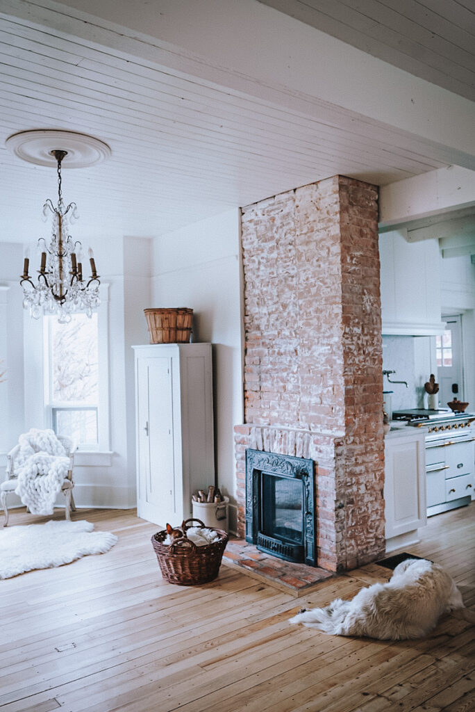 A stunning view of an exposed brick fireplace with beautiful hardwood floors and two dogs lying in front of the fireplace in a calm home.