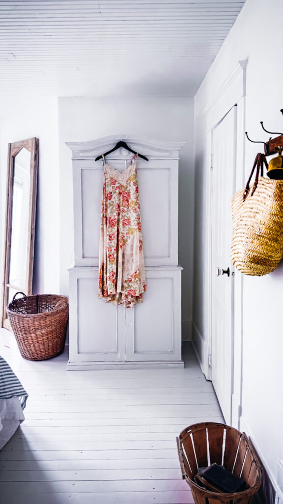 A calm bedroom area with painted floors and furniture, but lots of natural texture and a dress hanging from the armoire.
