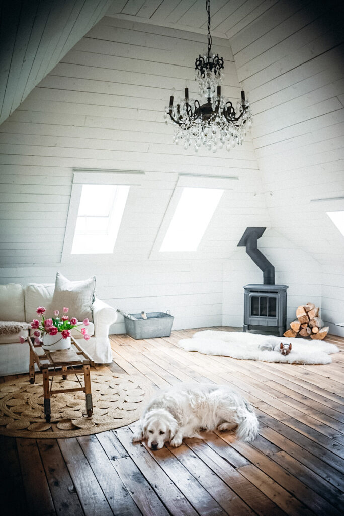 A beautiful, calming attic space in a home that has a wood burning fireplace and a large chandelier hanging from the ceiling.